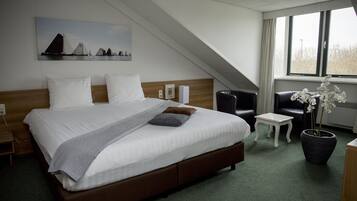 A hotel room with a large bed, a small table, a chair, a potted plant, and a painting on the wall.
