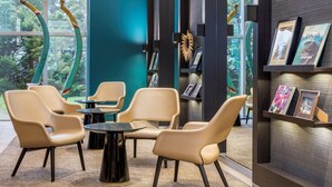 A modern interior with beige chairs around a small table, a teal accent wall, and a bookshelf with framed items. - Best Western Plus Hotel Admiral (La Tour-de-Salvagny)