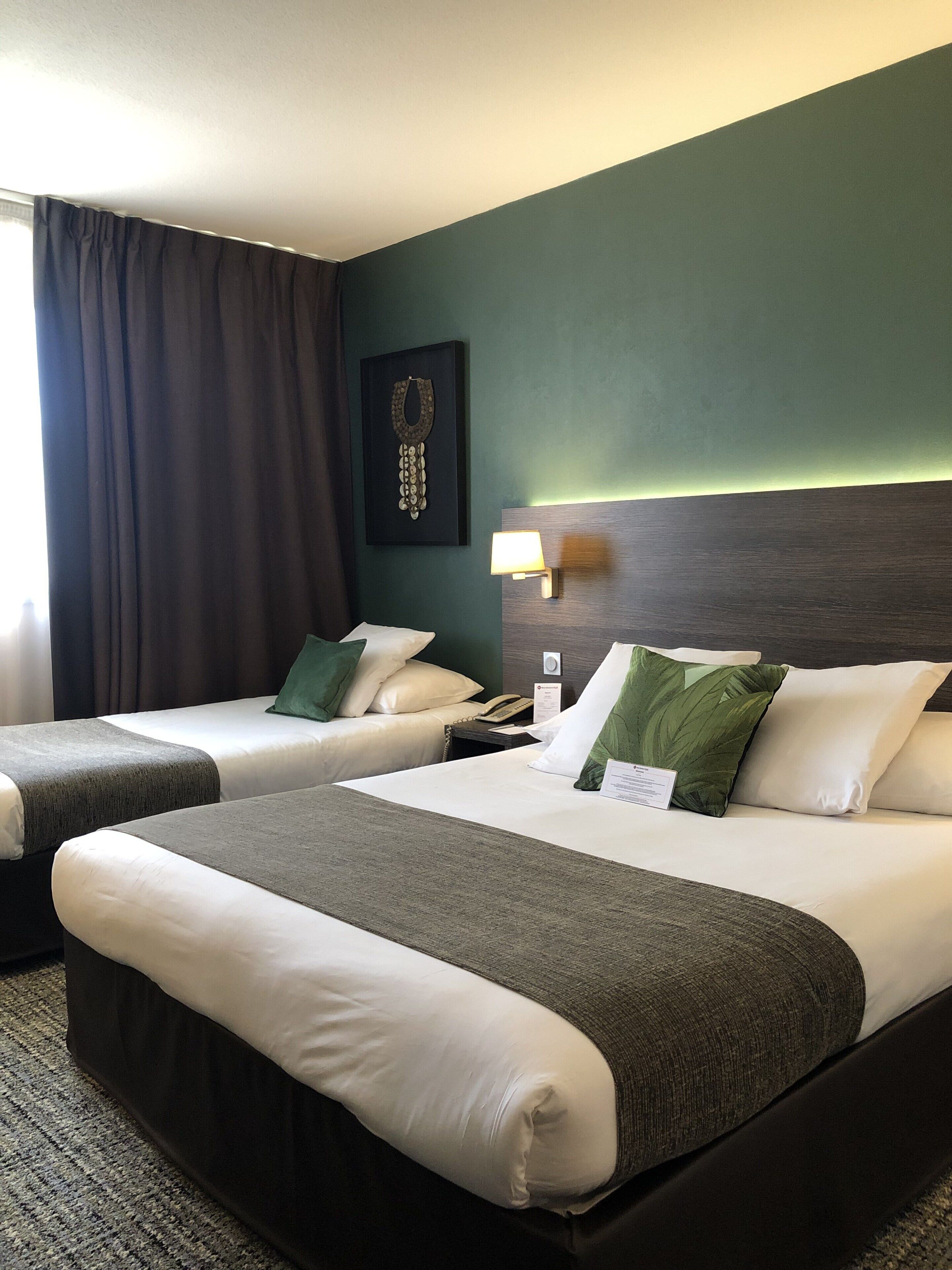 A hotel room with two beds, a dark green wall, a framed artwork, a bedside lamp, and a telephone.