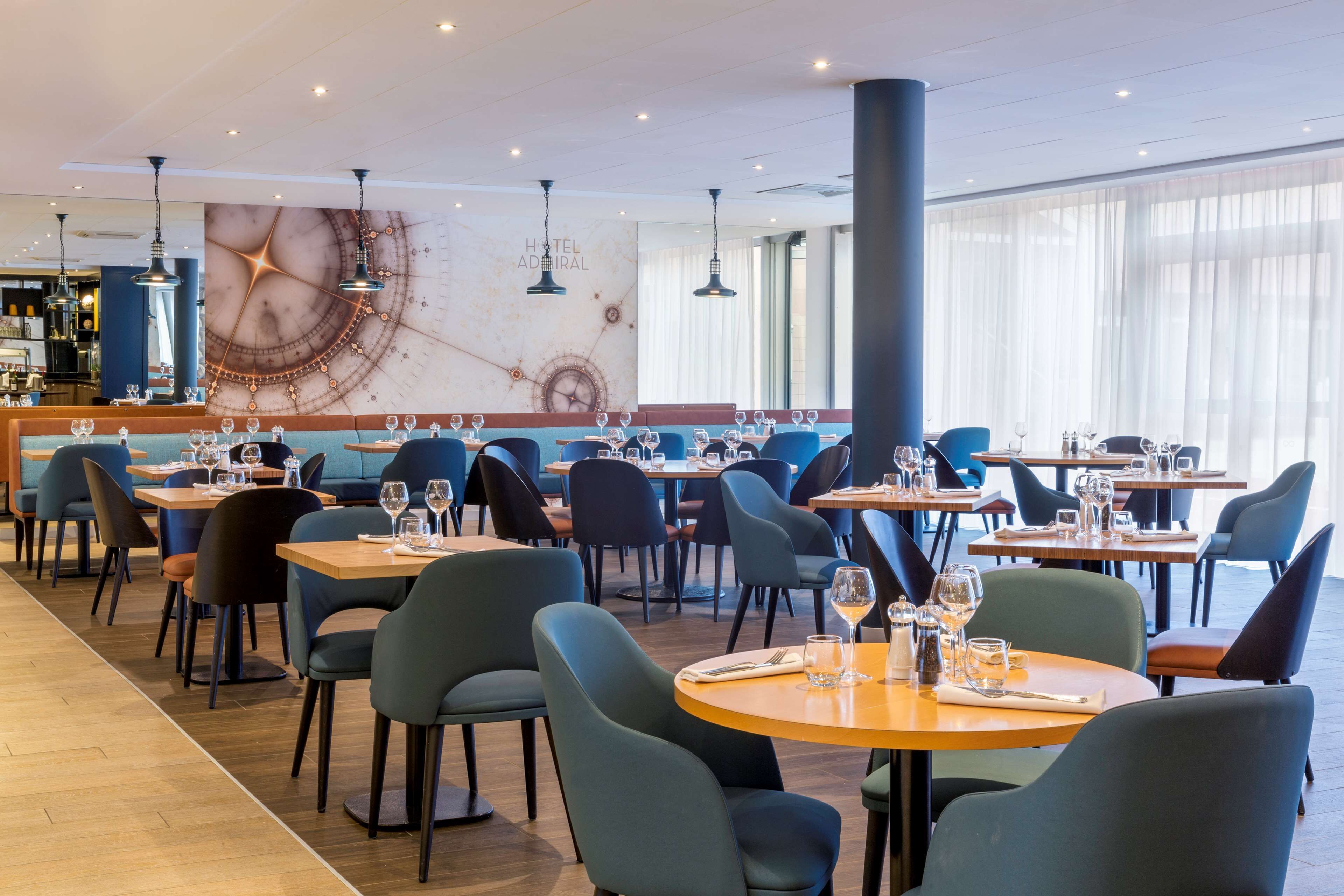 A modern restaurant with round tables and blue chairs, a marble wall with a clock, and a bar area.