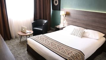 A hotel room with a bed, a chair, a small table with a laptop, a lamp, and a wall decoration.