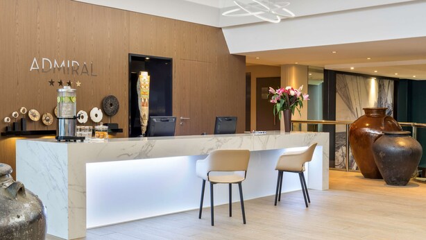 A modern reception area with a marble counter, two chairs, and a large vase with flowers. - Best Western Plus Hotel Admiral (La Tour-de-Salvagny)