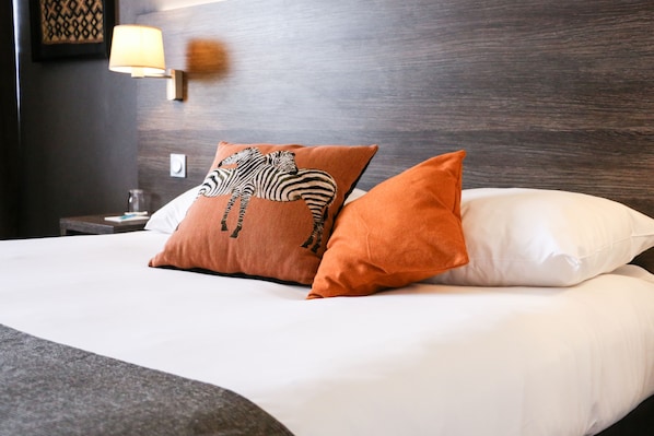 A neatly made bed with white and orange pillows, a wooden headboard, and a wall-mounted lamp.