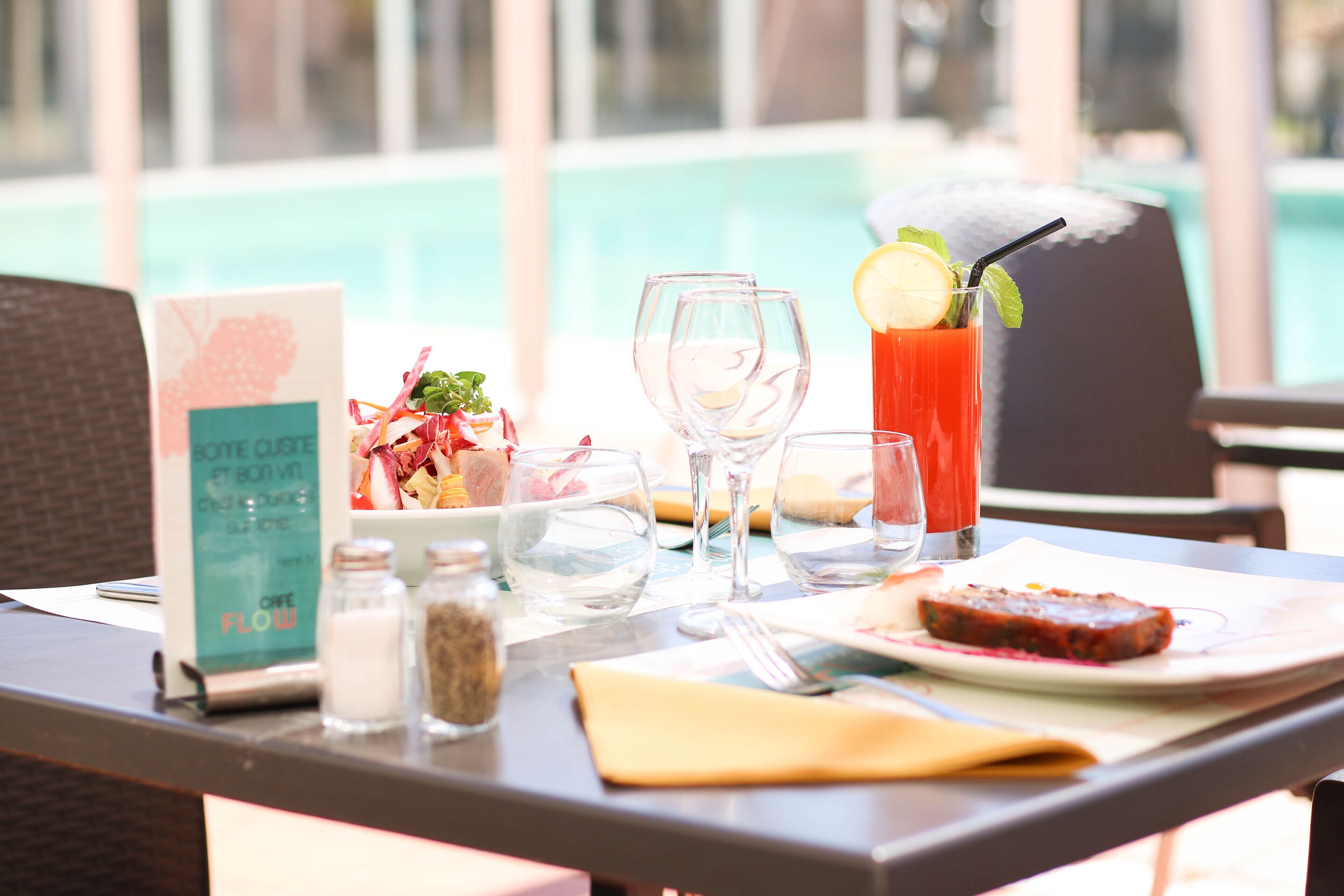 Une table à manger avec un menu, des verres, un verre d’une boisson rouge, une part de gâteau, ainsi qu’un salier et un poivrier.