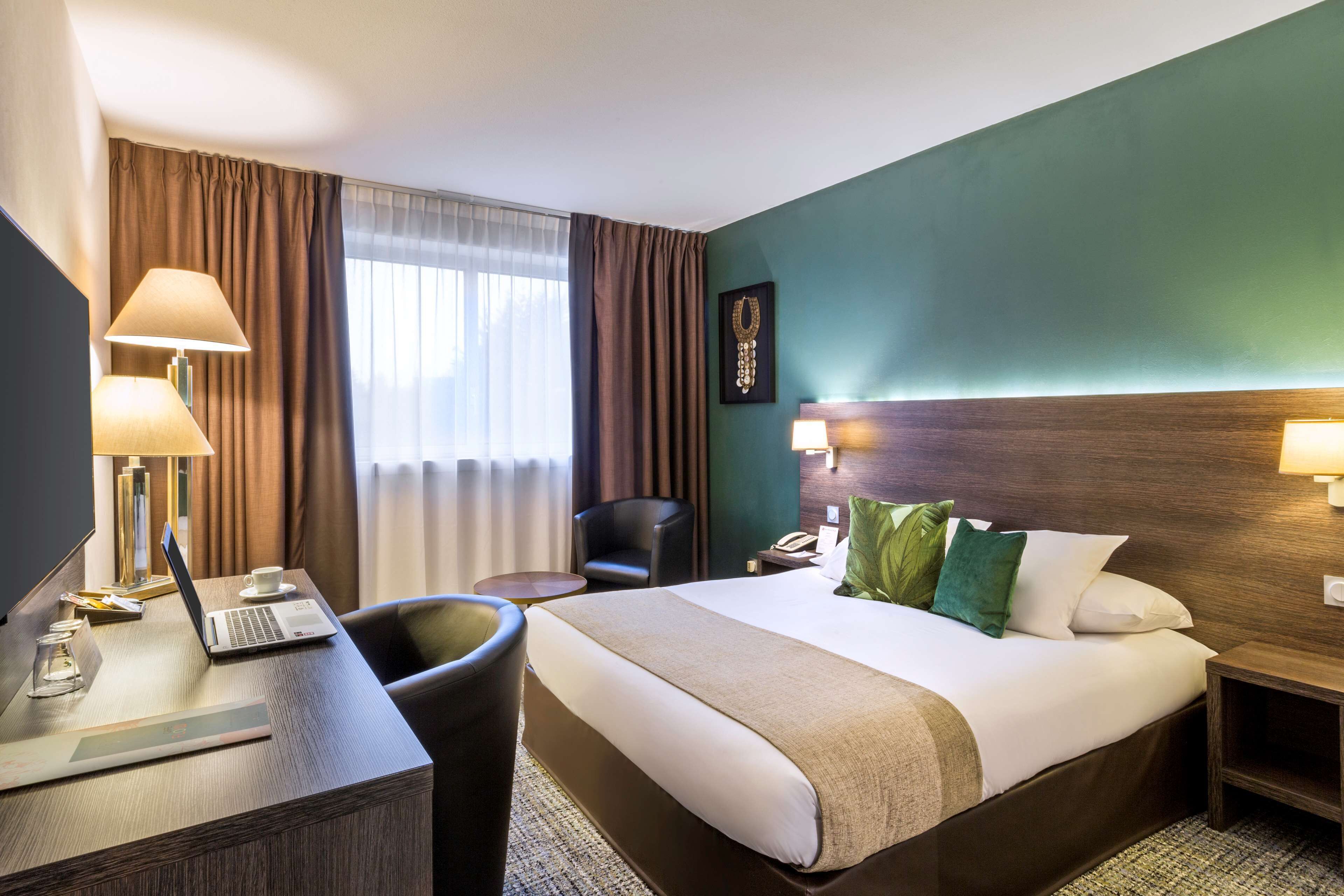 Habitación de hotel con cama, escritorio, silla, lámpara y vistas al exterior a través de la ventana.