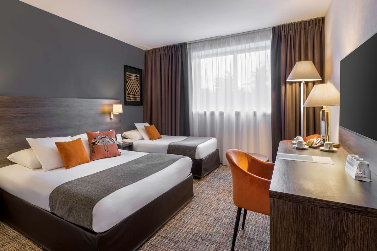 A hotel room with two beds, a desk, a chair, a lamp, and a window with curtains.