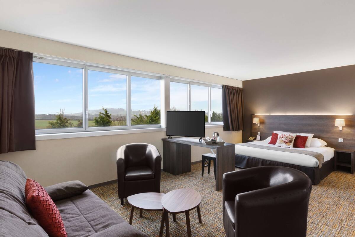 A hotel room with a large bed, a desk, a TV, and a view of the outdoors.