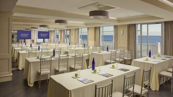 A conference room with multiple tables, chairs, and large windows offering a view of the ocean.