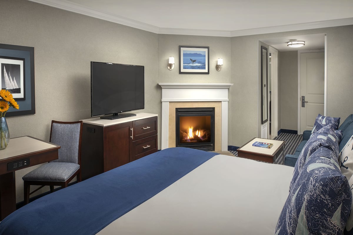 A hotel room with a bed, a desk with a TV, a fireplace, and a door leading to another room.