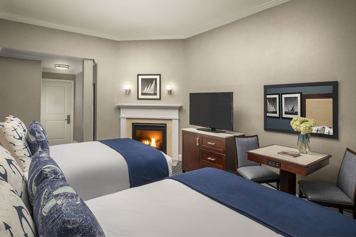 A hotel room with two beds, a fireplace, a TV, a desk with a chair, and a mirror on the wall.