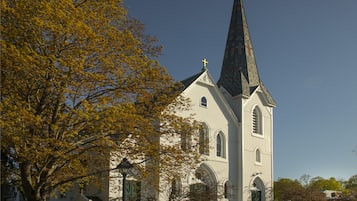 A church with a tall steeple and a cross on top, surrounded by trees with yellow leaves.