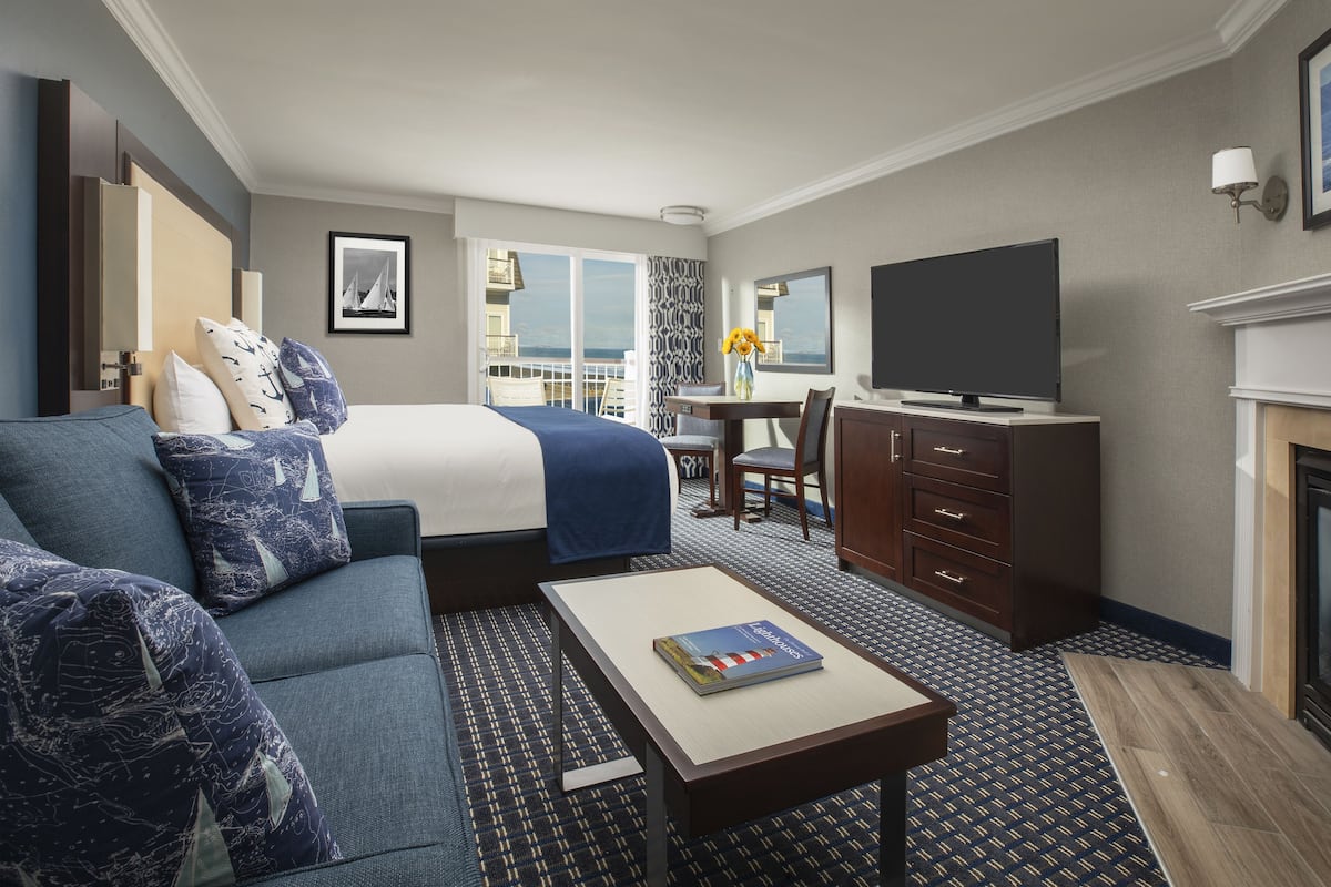 A hotel room with a bed, a sofa, a TV, a desk, and a fireplace.