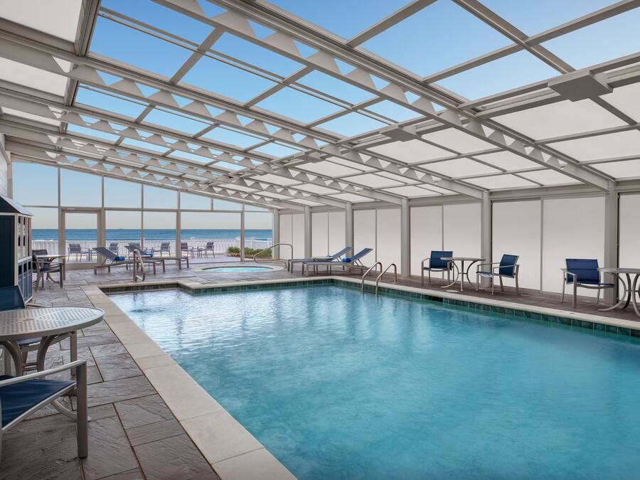 Piscina interior con vistas claras al océano, rodeada de sillones y mesas.
