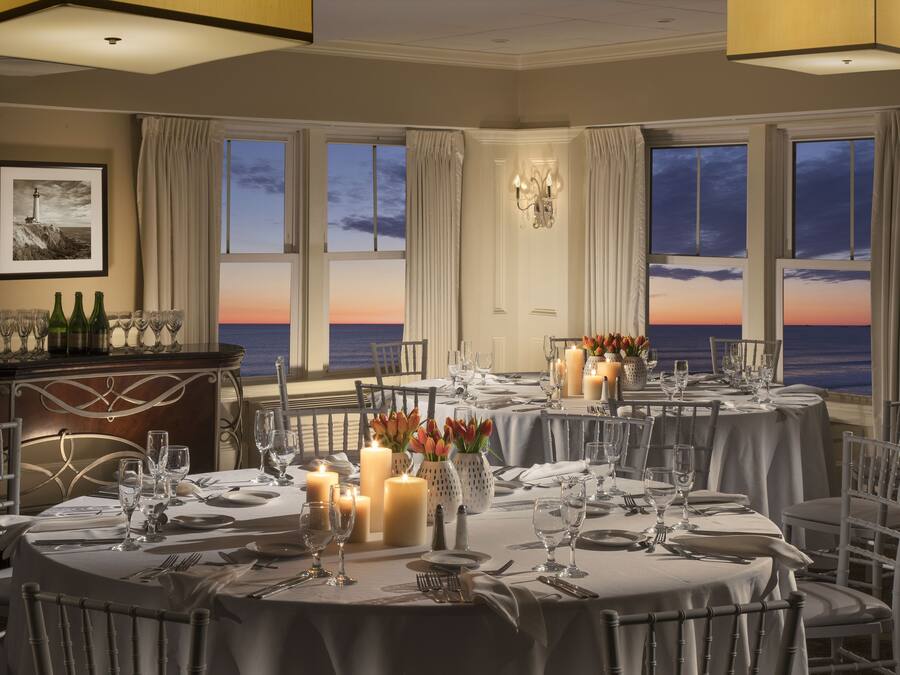 A dining area with tables set for a meal, candles, and a view of the ocean at sunset.