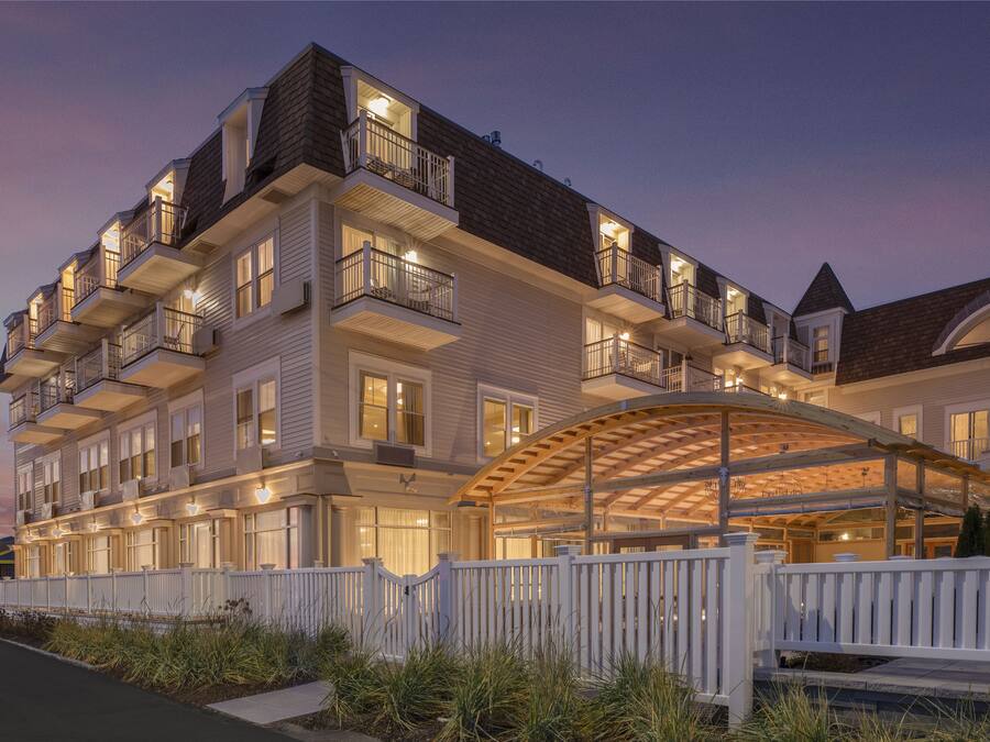 A multi-story hotel with balconies, a covered outdoor area, and a white fence.