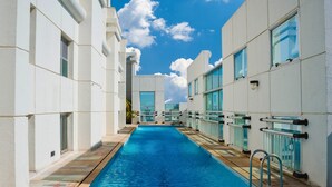 Una piscina con agua azul cristalina, rodeada de edificios blancos con grandes ventanales y un cielo nublado.