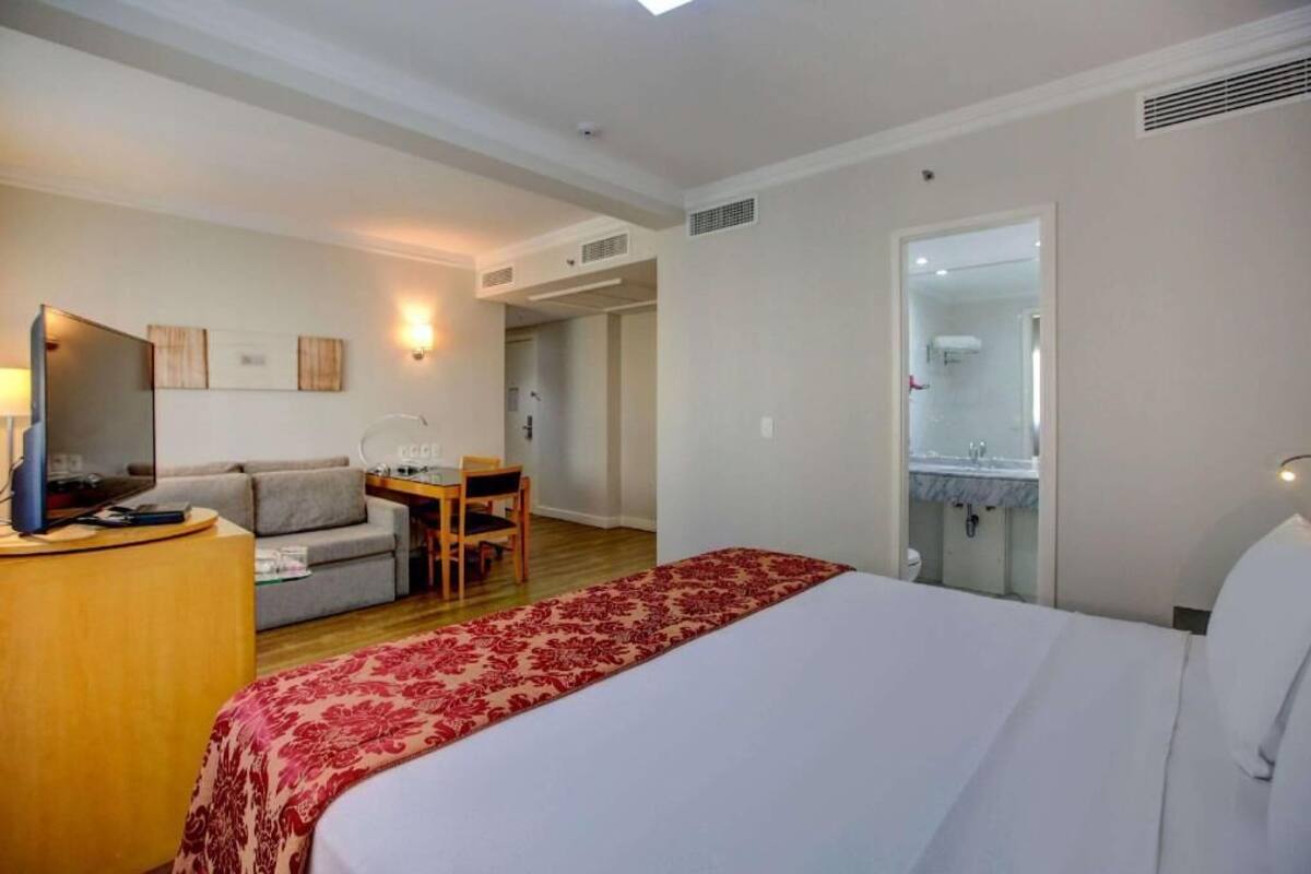 Ett hotellrum med en säng, ett skrivbord, en soffa och ett badrum som syns genom en öppen dörr.