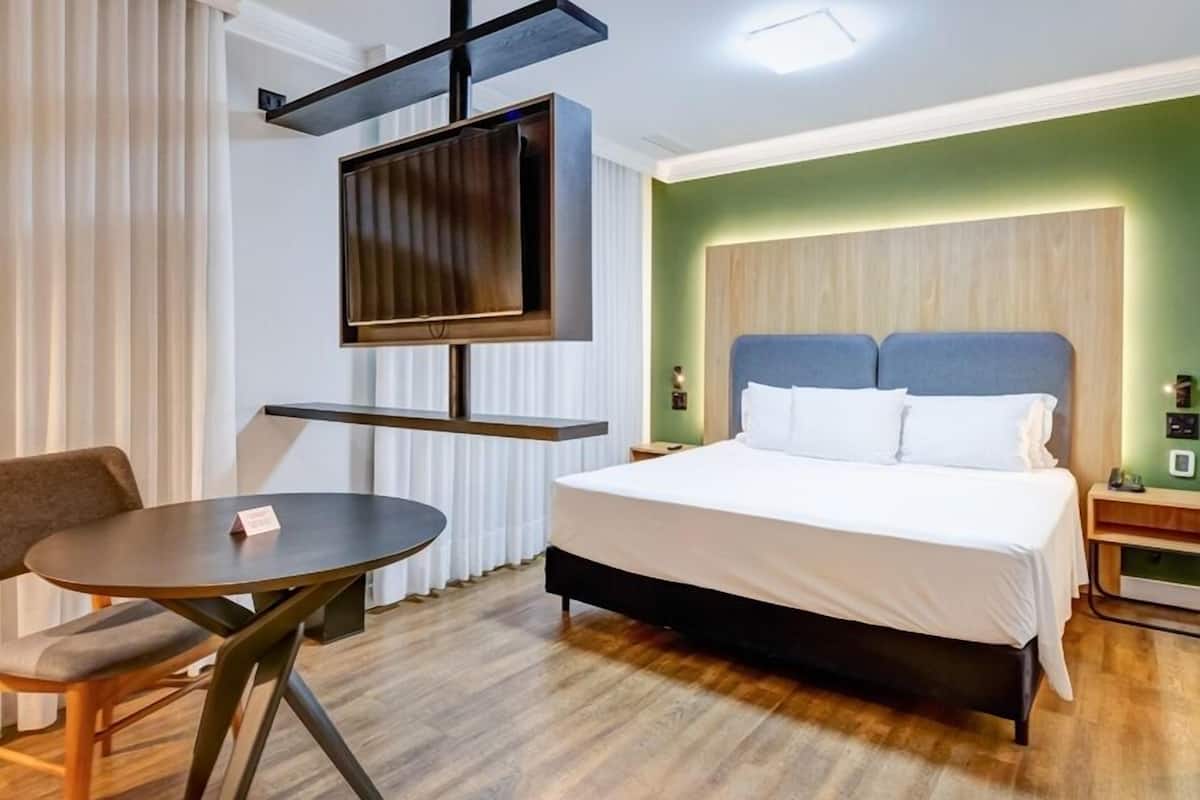Ett hotellrum med en säng, en tv som är monterad på väggen, ett bord och en stol.