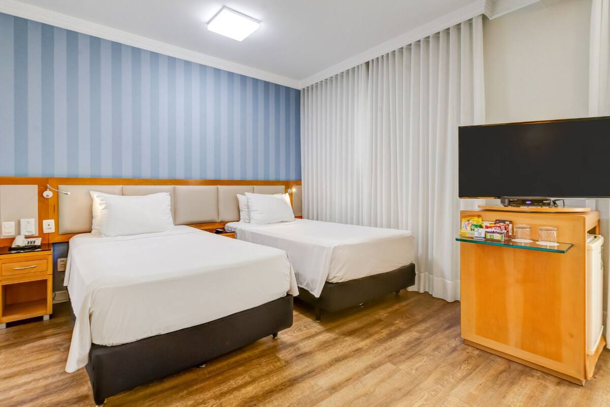 A hotel room with two beds, a TV, a minibar, and a wooden floor.