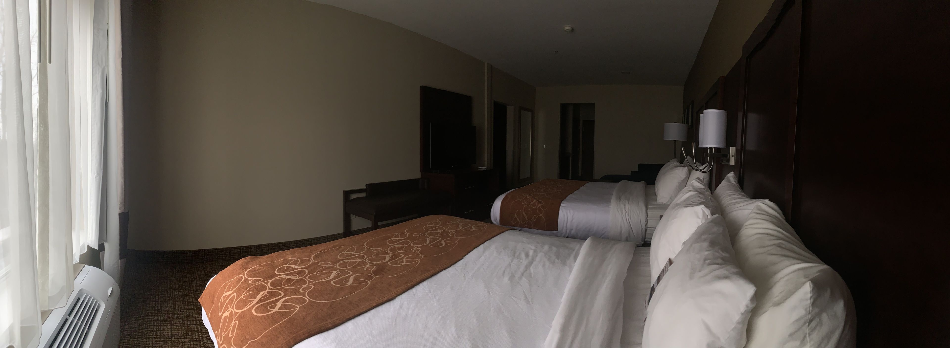 A hotel room with two beds, a desk, and a large window with curtains.