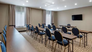 Un salón de conferencias con una larga mesa y sillas, un televisor de pantalla plana y ventanas grandes con cortinas.