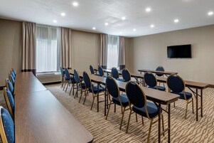 Un salón de conferencias con una larga mesa y sillas, un televisor de pantalla plana y ventanas grandes con cortinas.
