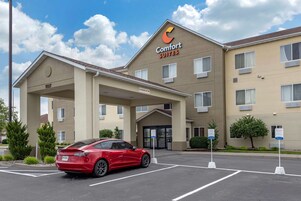 Un hotel Comfort Suites con estacionamiento y un coche rojo aparcado delante.