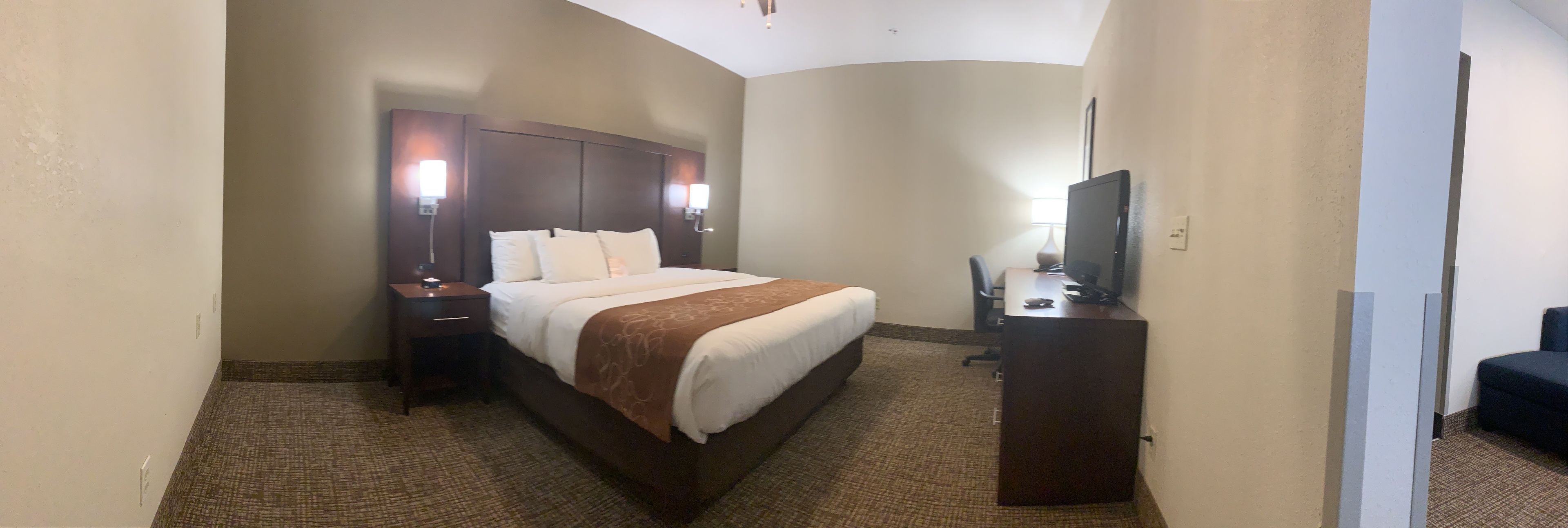 A hotel room with a bed, bedside tables, a desk, and a television.