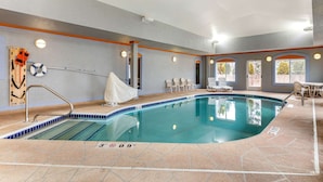 An indoor swimming pool with clear lane markings, a lifeguard chair, and a covered seating area.