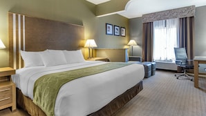 A hotel room with a large bed, bedside lamps, a desk, a chair, and a window with curtains.