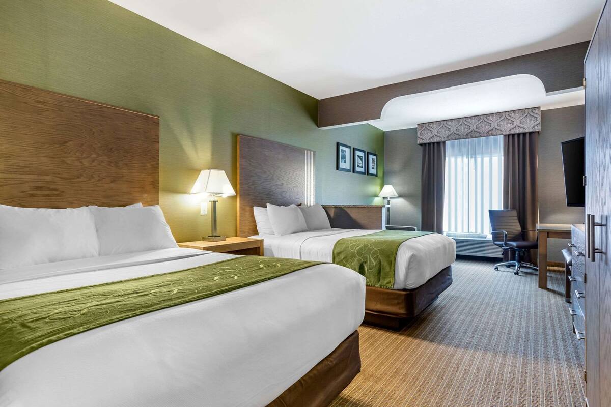 A hotel room with two beds, a desk, a chair, and a television.