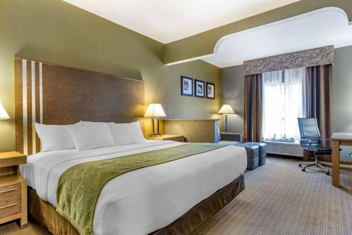Hotellihuone, jossa on suuri sänky, kaksi yöpöytää, työpöytä tuolilla sekä suuri ikkuna, jossa on verhot.