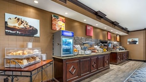 A hotel breakfast area with a self-service station, a refrigerator with beverages, and a variety of food items.