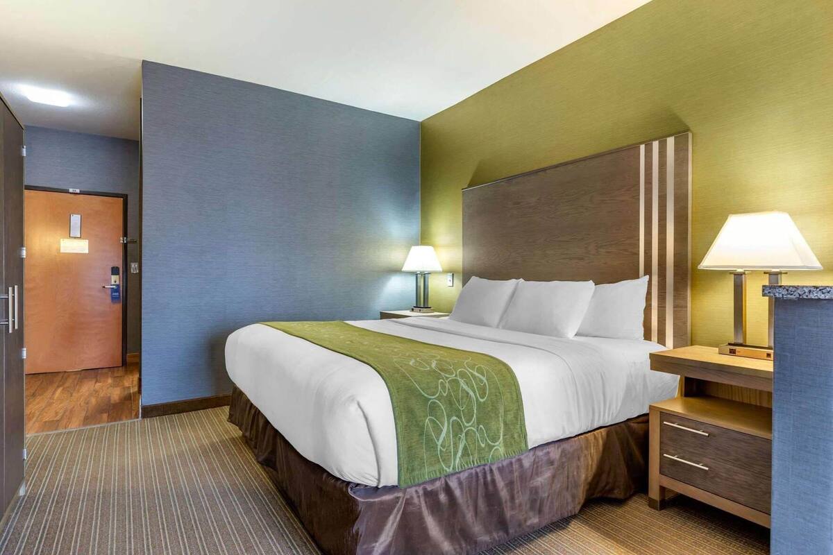 A hotel room with a bed, bedside tables, lamps, and a door.