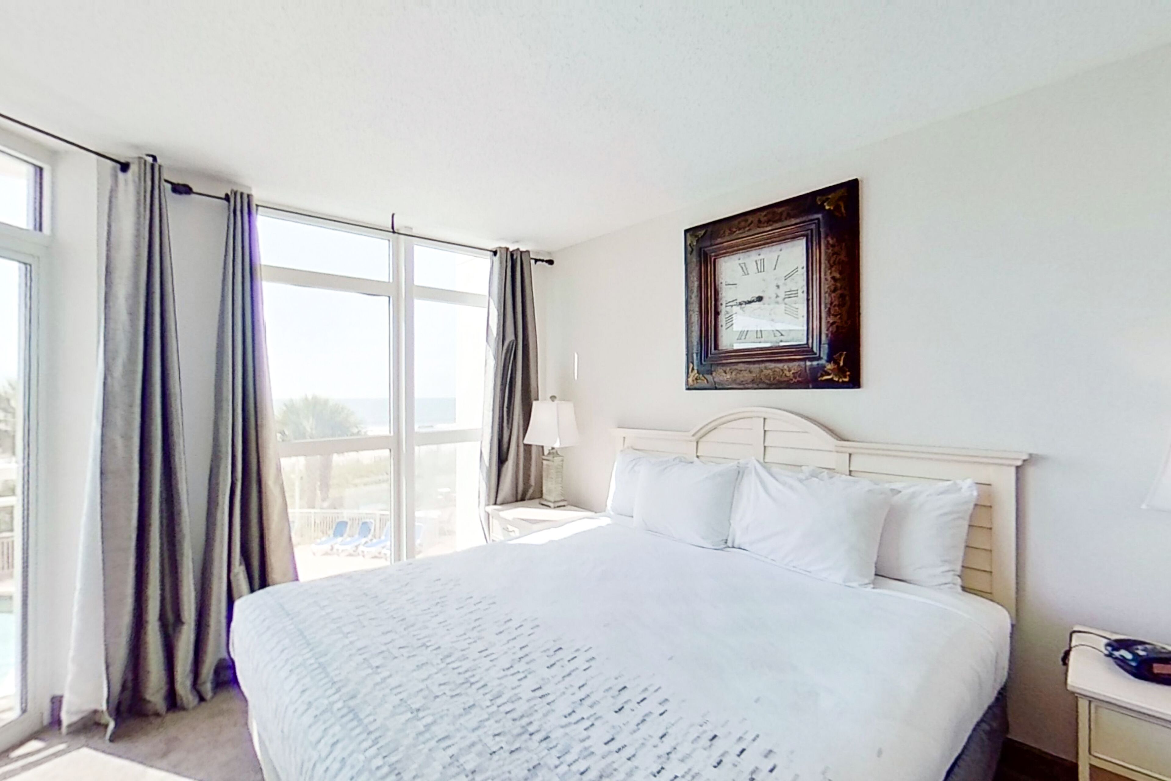A hotel room with a large bed, a nightstand, a lamp, and a wall clock.