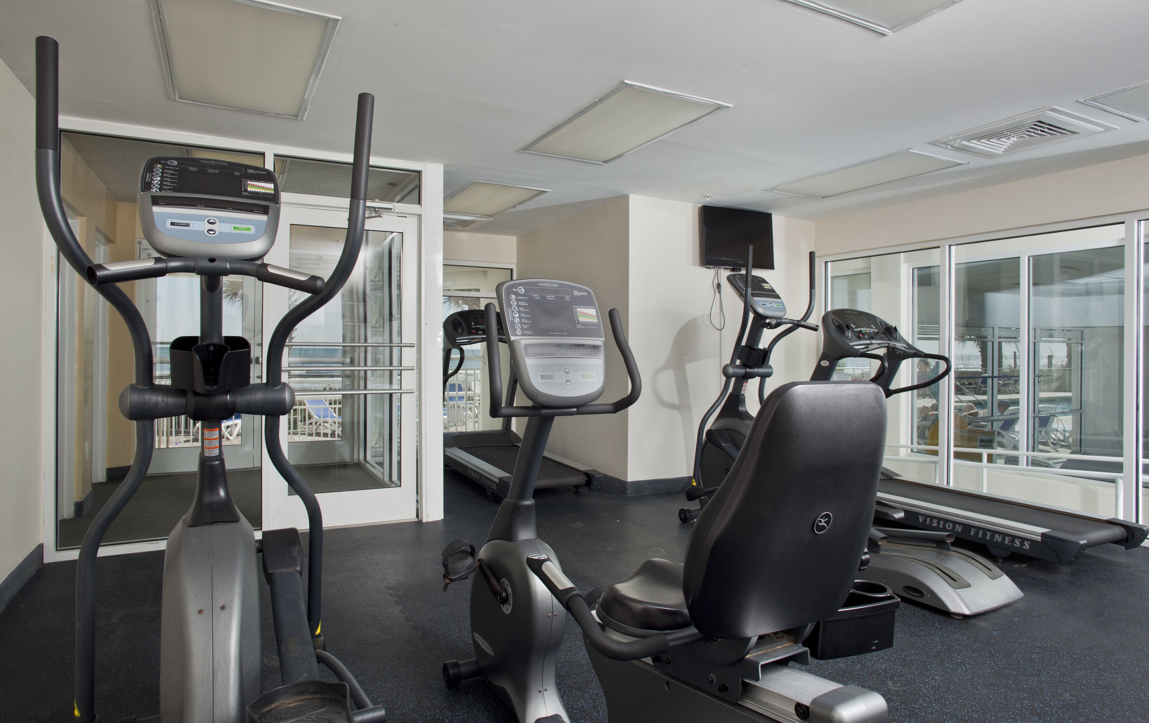 Ein Fitnessraum mit verschiedenen Trainingsgeräten, darunter Laufbänder, ein Crosstrainer und ein Ergometer.