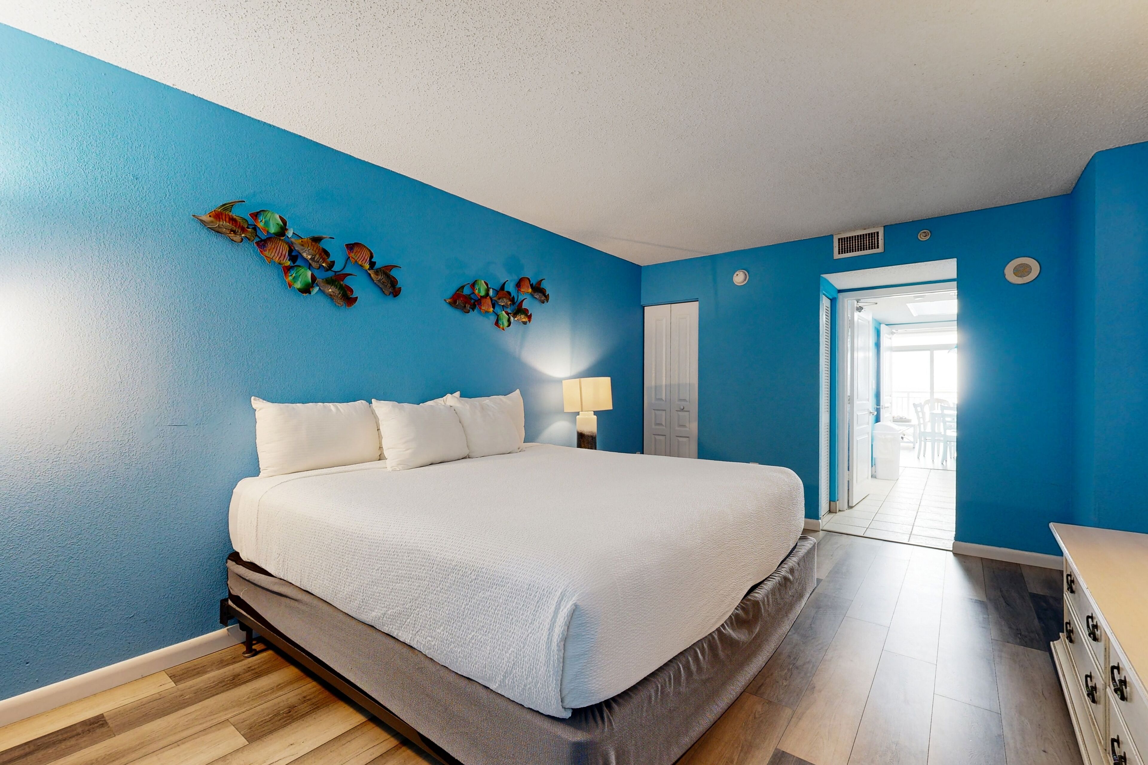 A bedroom with a large bed, blue walls, and a wooden floor.