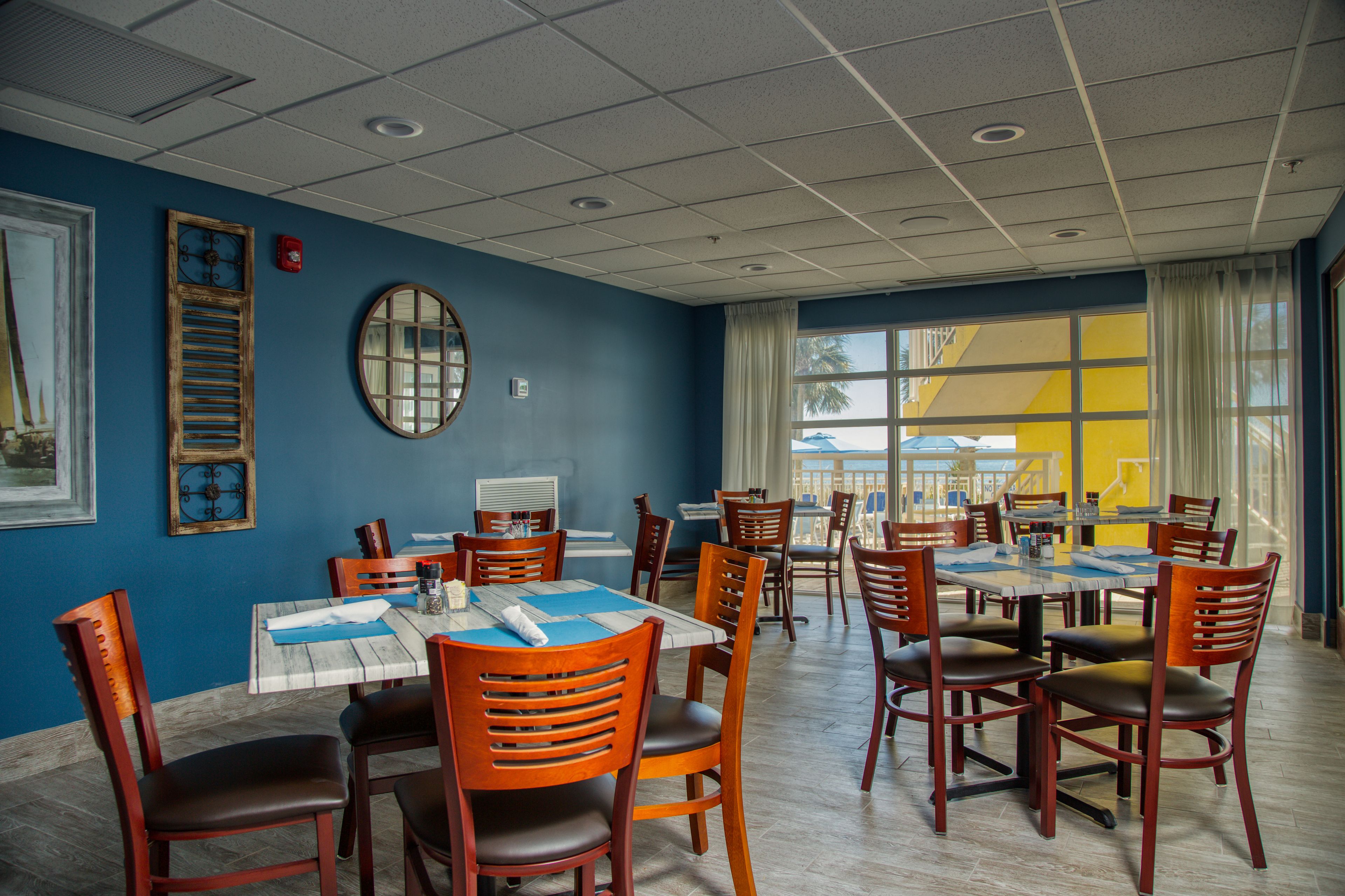 A dining area with multiple tables and chairs, a clock, and a window with a view.