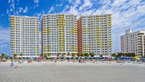 A beachfront hotel with multiple high-rise buildings, a sandy beach, and numerous colorful umbrellas.