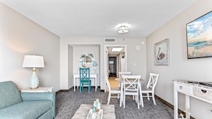 A modern living room with a teal sofa, a white coffee table, and a dining area with white chairs and a table.
