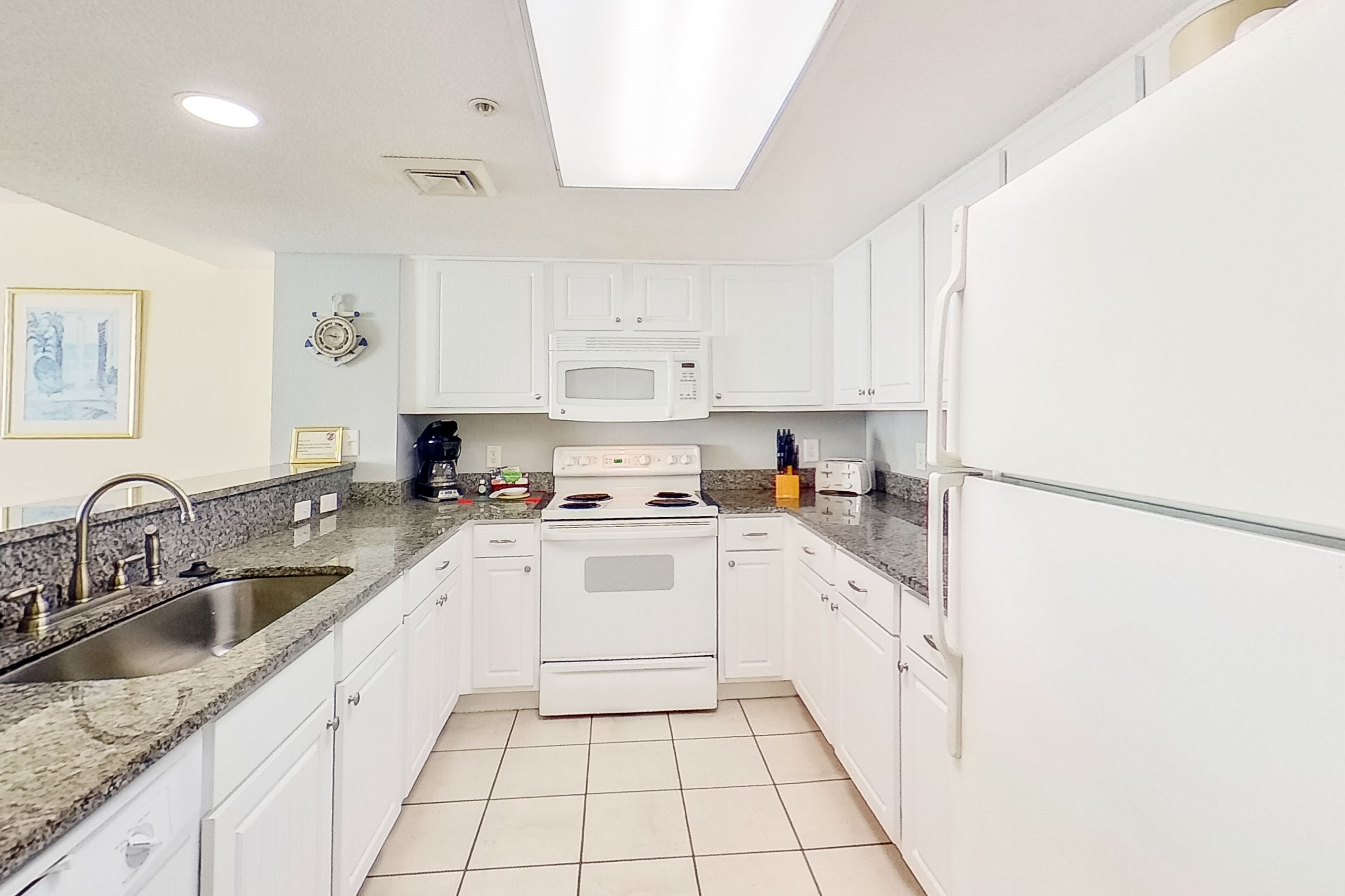 A kitchen with white cabinets, a granite countertop, a stainless steel sink, a microwave, a stove, and a refrigerator.