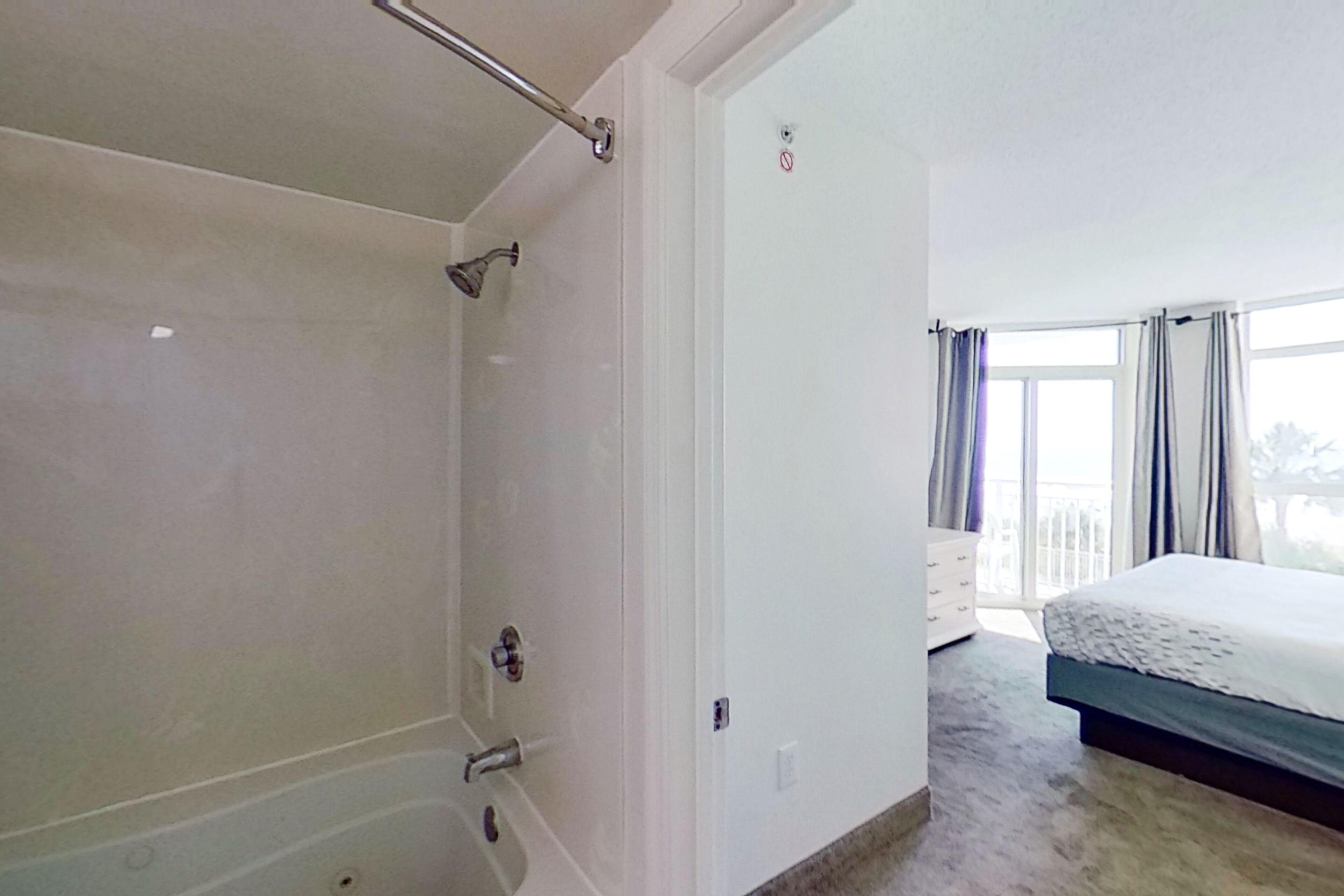 A bedroom with a large bed, a shower, and a view of the outdoors through a window.