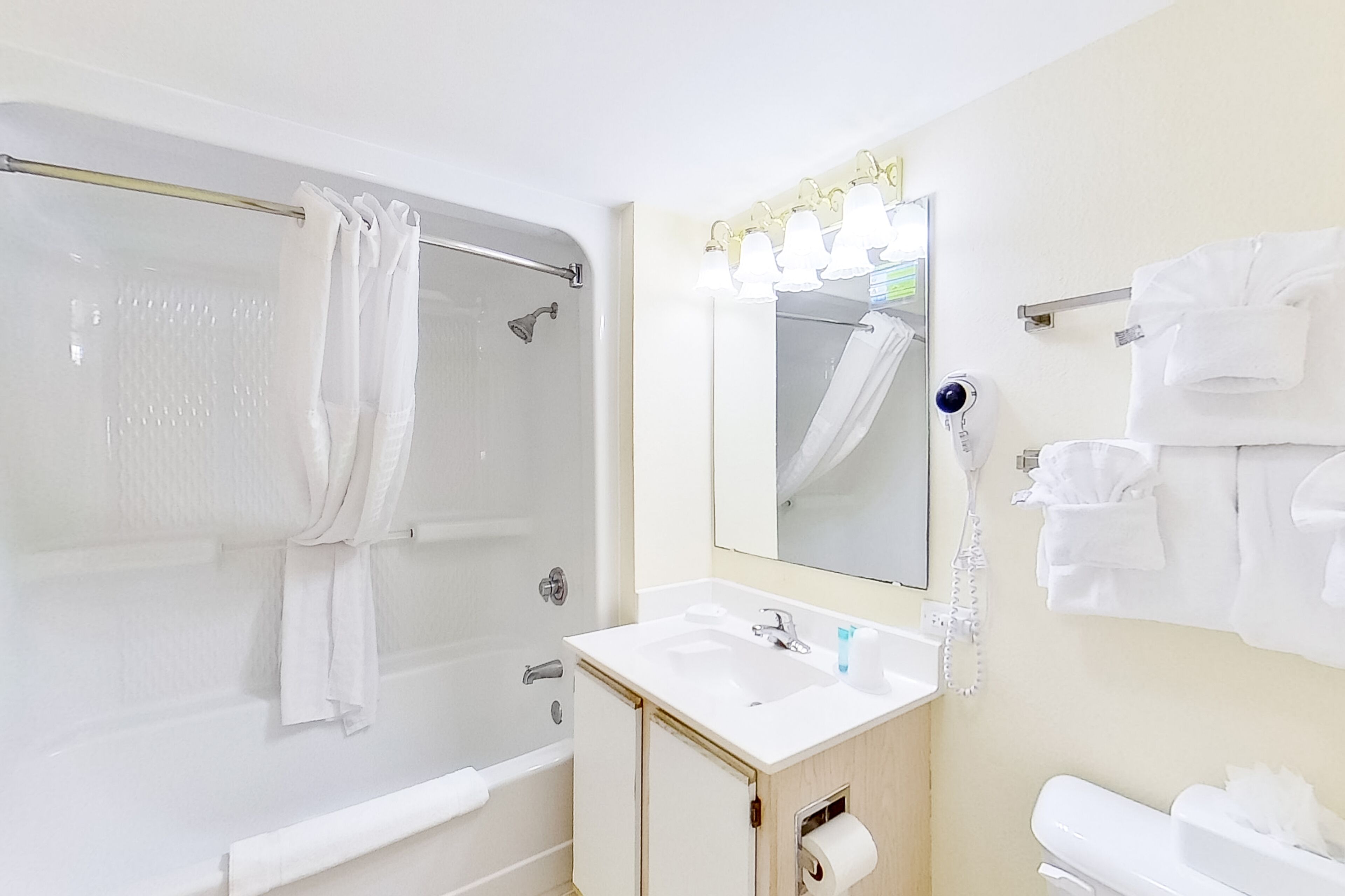 A bathroom with a bathtub, a sink, a mirror with lights, and a towel rack.