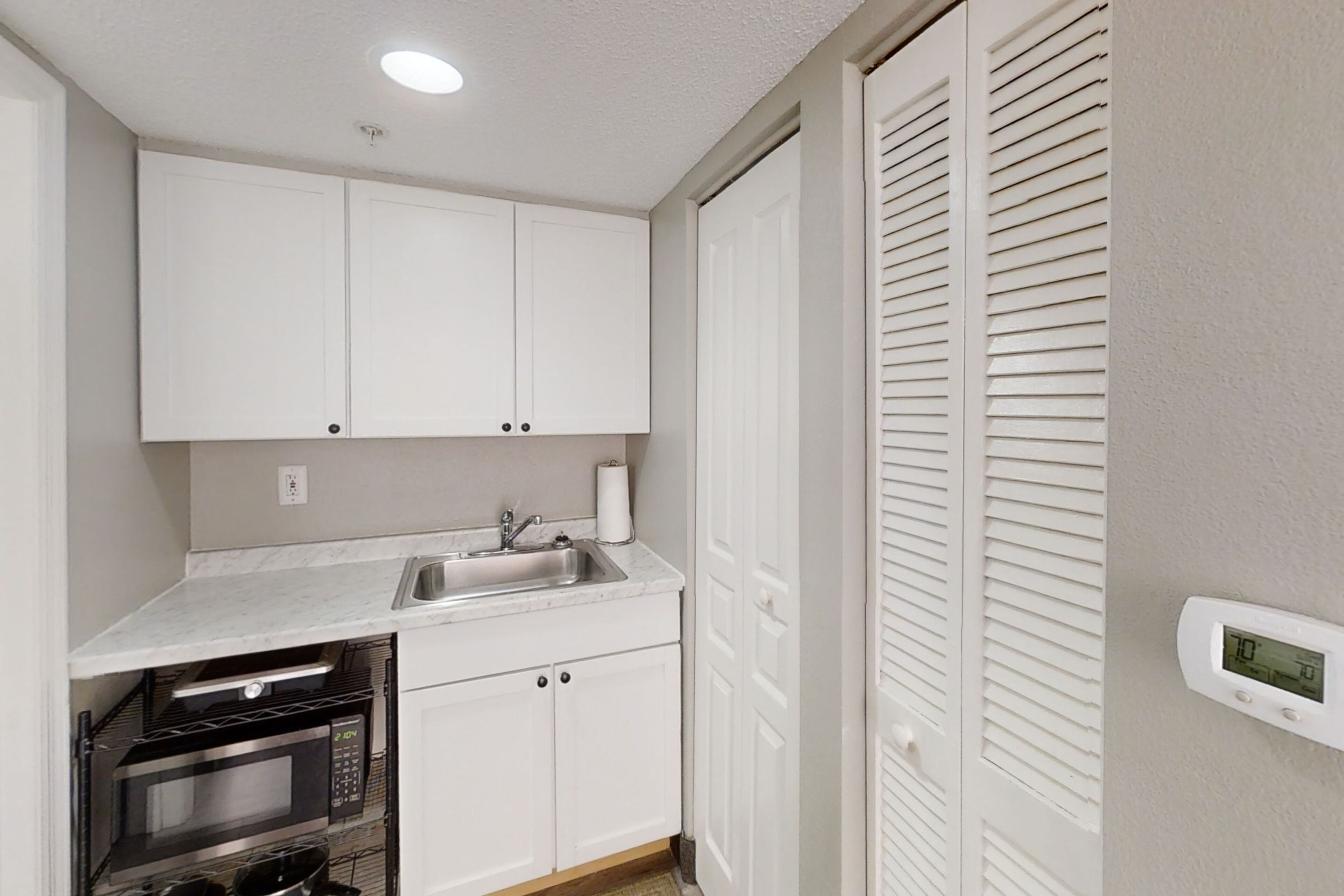 A compact kitchen with white cabinets, a built-in oven, and a digital thermostat.