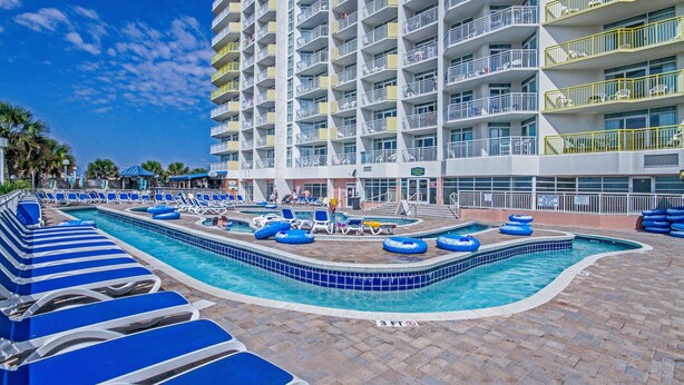 A hotel pool area with blue lounge chairs and inflatable rings, surrounded by a multi-story building with balconies.