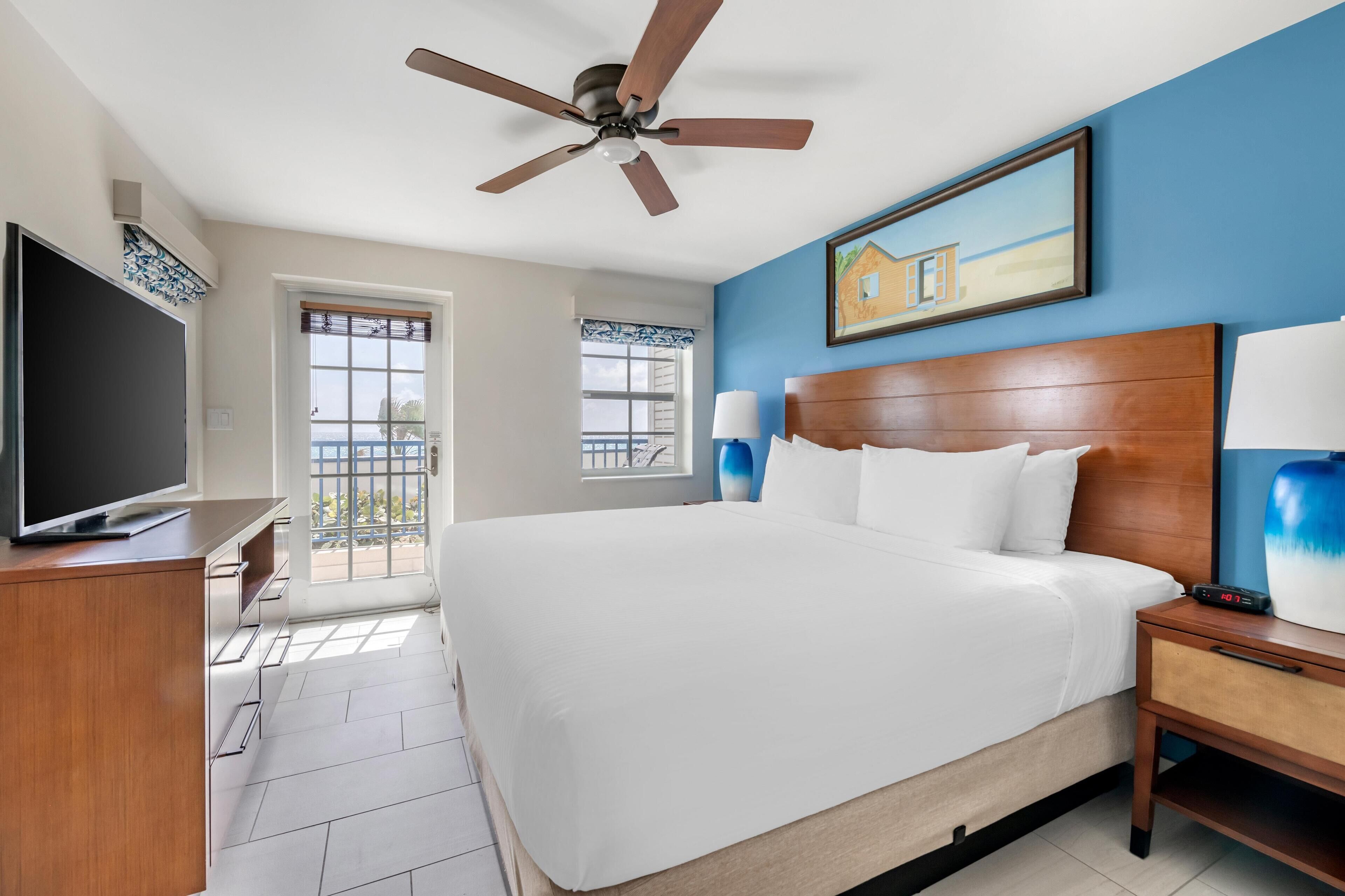 Habitación de hotel con una cama grande, ventilador de techo, televisión y ventana con vista al exterior.