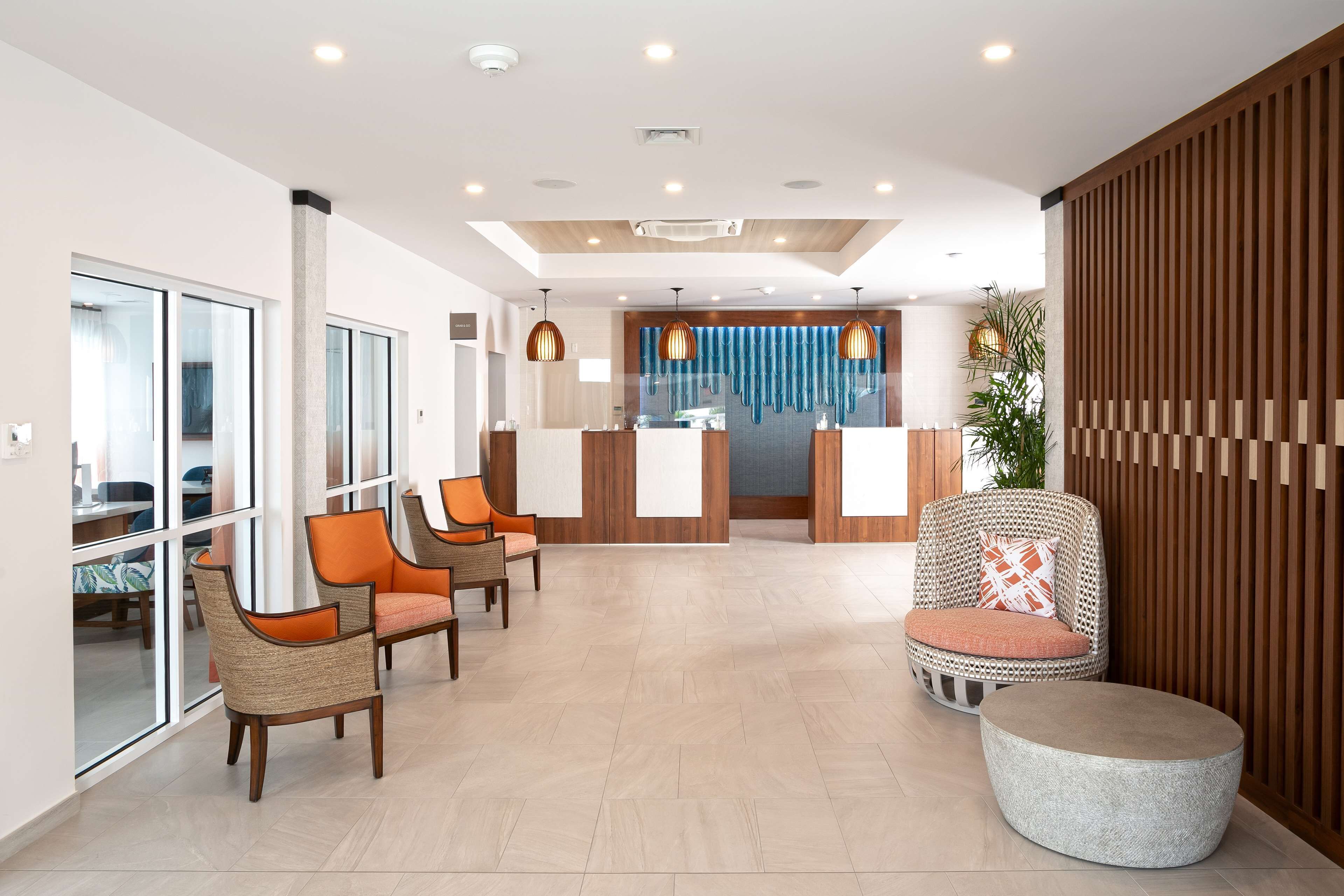 A modern reception area with a reception desk, seating with orange cushions, and a large plant.