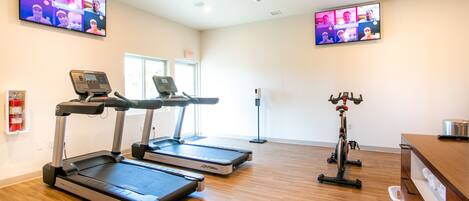 Gimnasio con cintas de correr, bicicleta estática y una televisión que muestra una clase virtual.