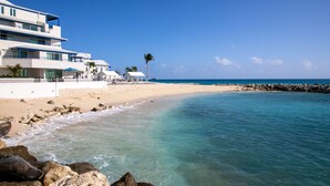 A beachfront hotel with a sandy beach, clear turquoise waters, and a rocky shoreline. - Hilton Vacation Club Flamingo Beach St. Maarten (Simpson Bay)