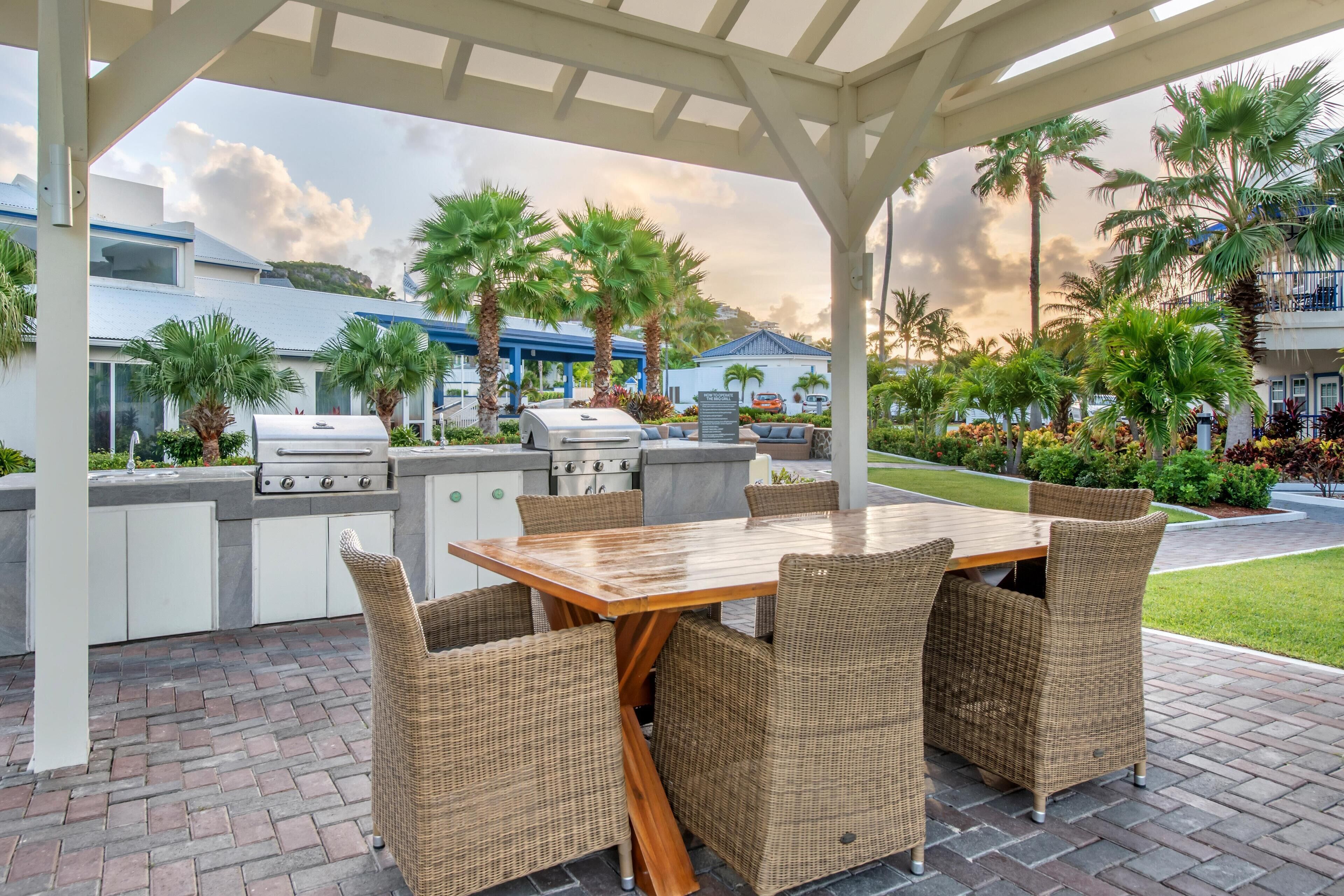 An outdoor patio with a grill, dining table, and wicker chairs.